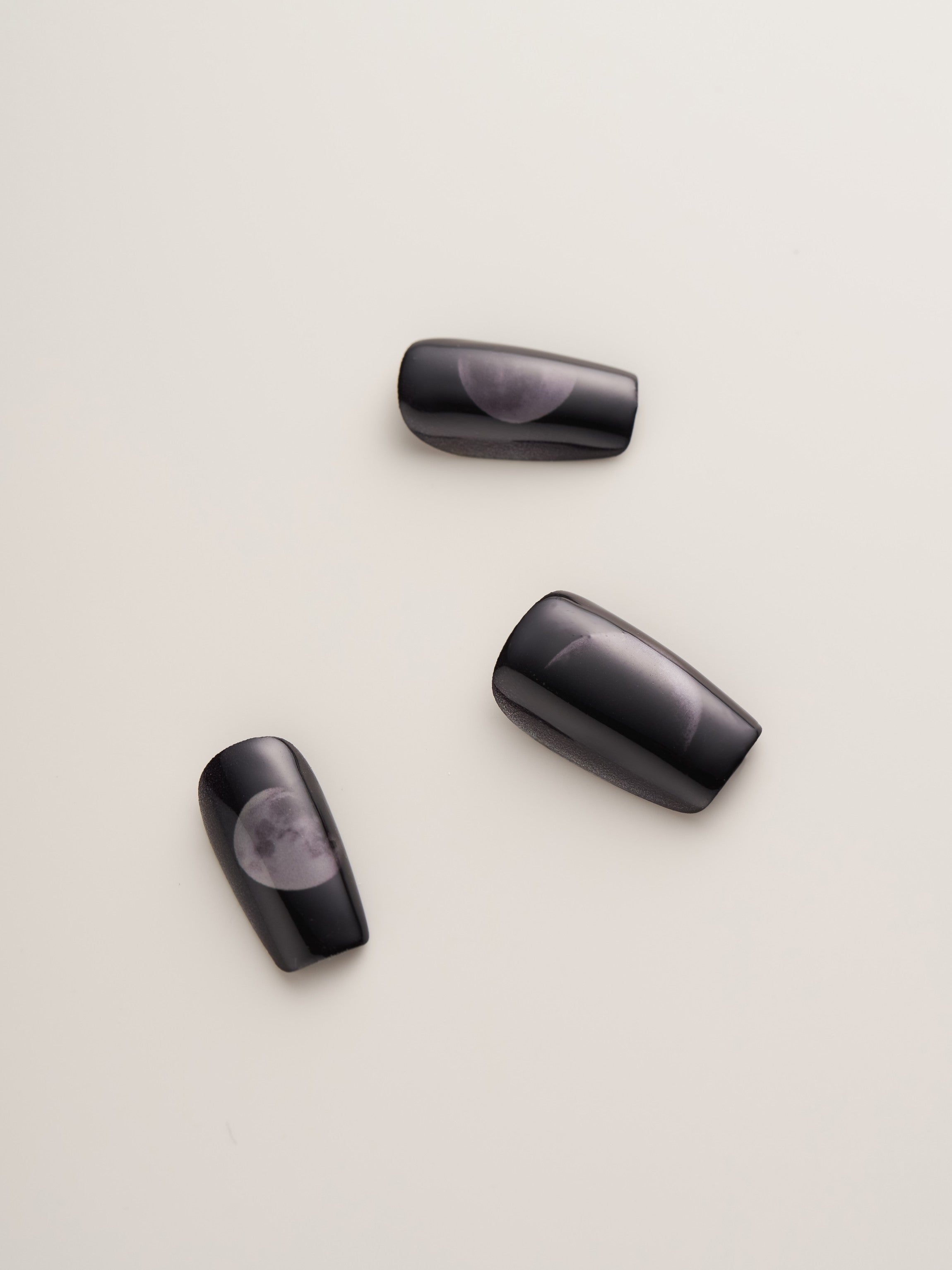 A collection of Mystical Moon Phases Squoval Press-On Nails in different sizes, highlighting celestial designs on a matte black finish, great for nail art lovers.