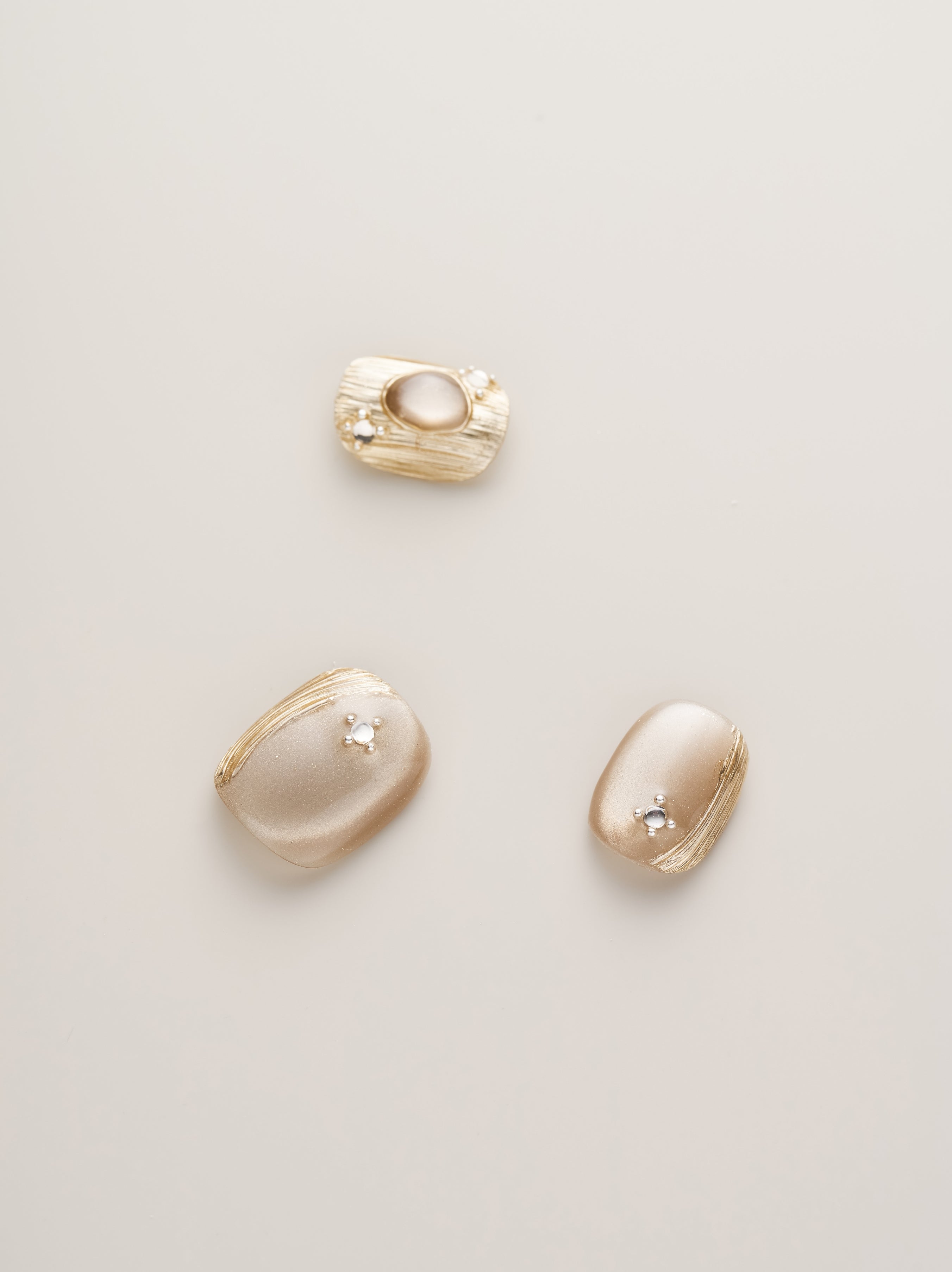 Close-up of Golden Luxe Metalli Squoval Press-On Nails showcasing three detailed nails with shimmering champagne gold and decorative accents.