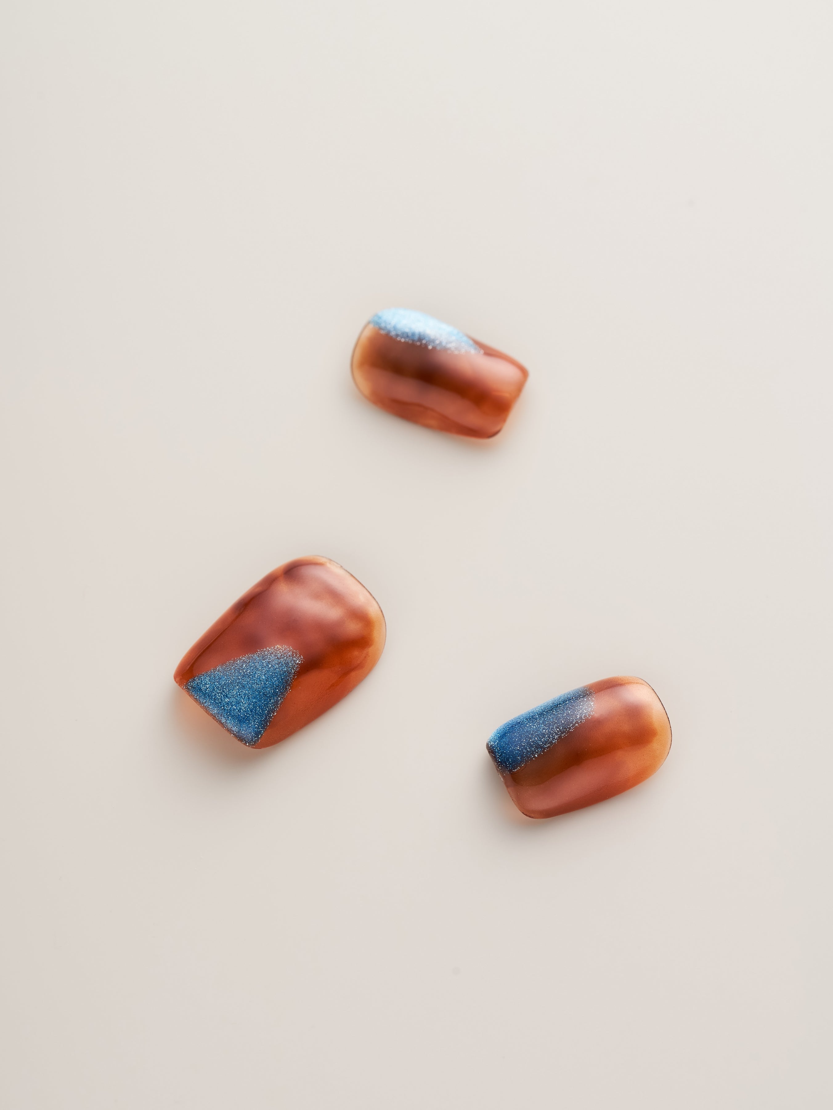 Three Amber Glow Squoval Press-On Nails displaying intricate amber designs enhanced with blue accent details.