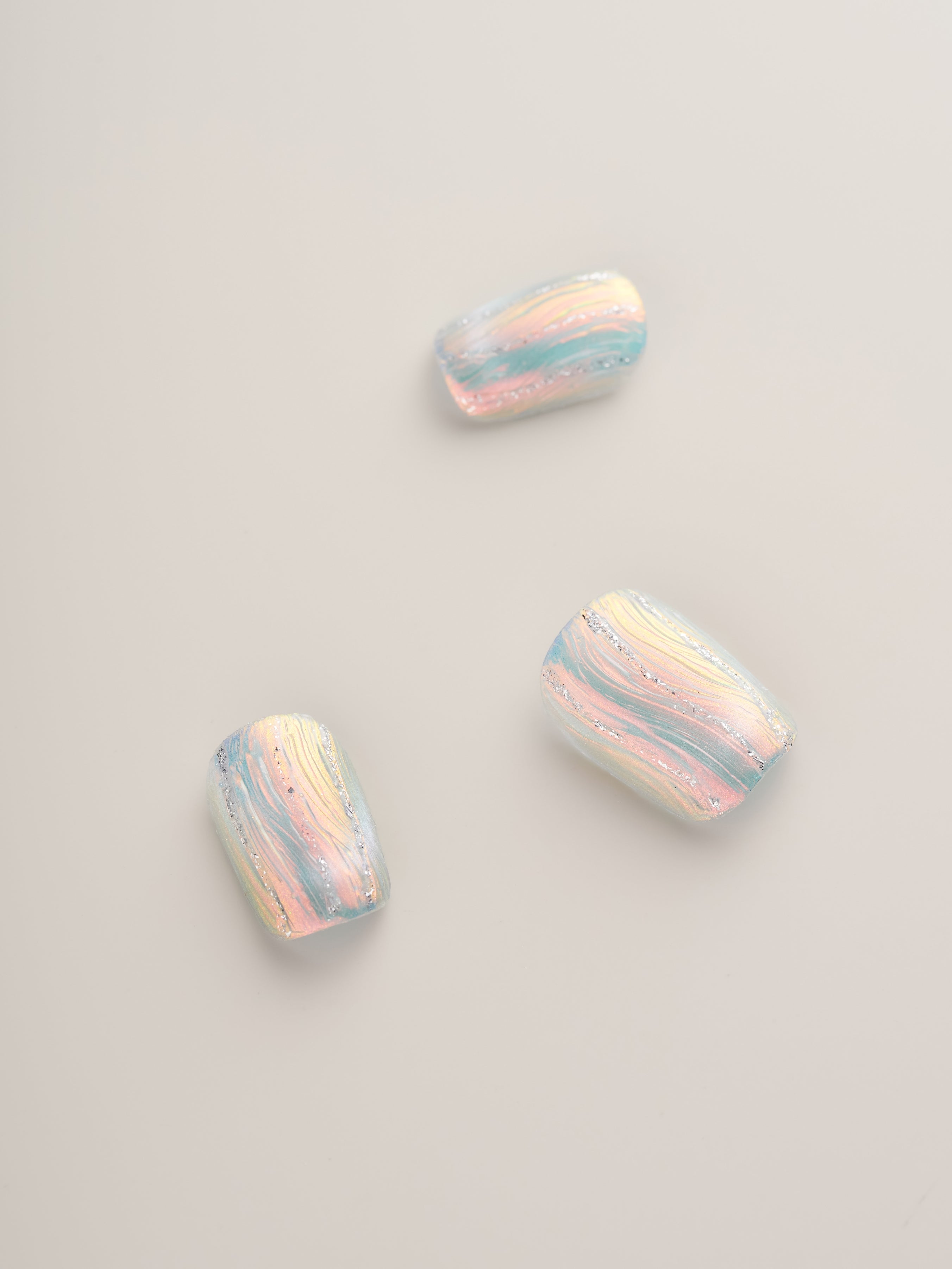 Close-up of Iridescent Frosted Squoval Press-On Nails highlighting three nails with a beautiful pastel iridescent finish and unique swirling designs.