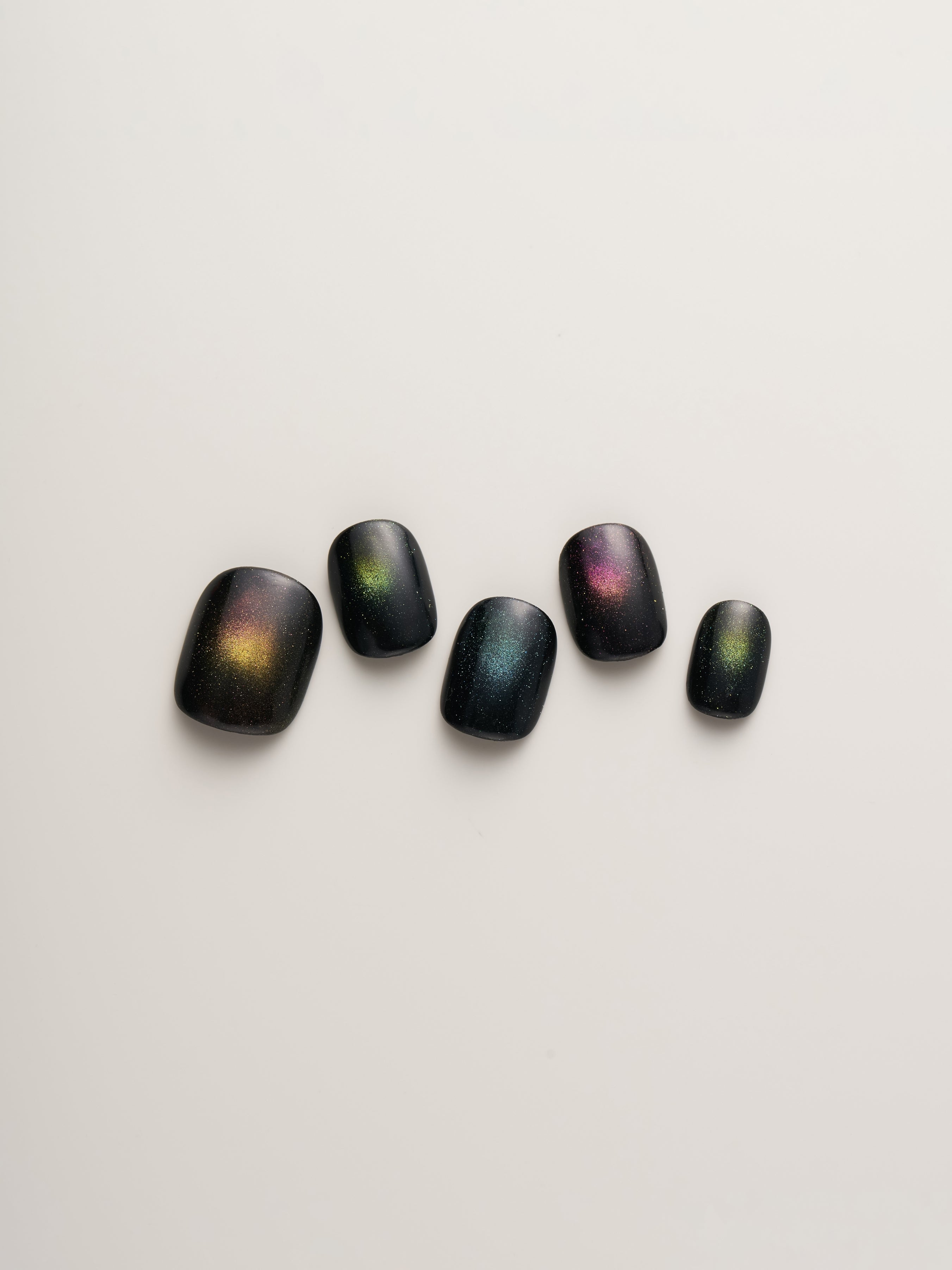 Arranged Cosmic Glow Square Press-On Nails displaying a selection of black nails with vibrant cosmic hues, offering an eye-catching nail art option.