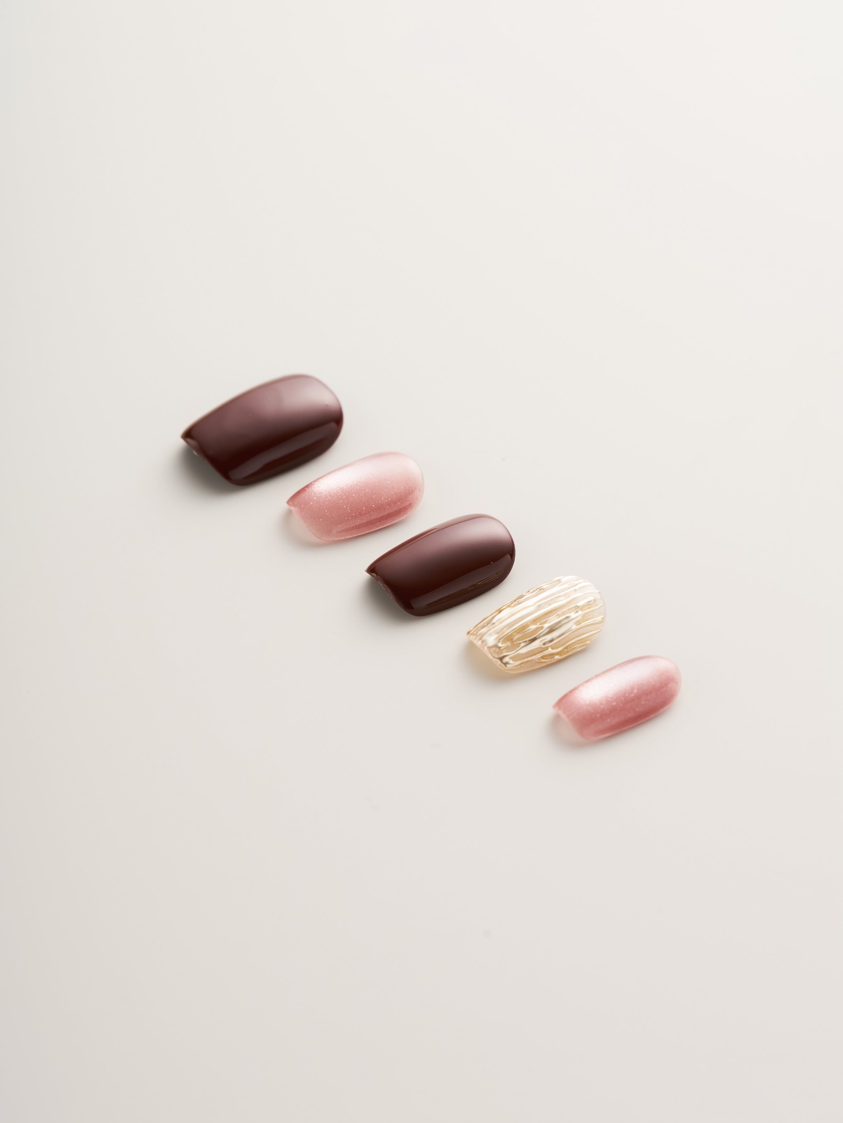 Close-up of Luxe Rosewood & Gold Textured Square Press-On Nails arranged elegantly, featuring deep rosewood, pink hues, and stylish gold textures for an upscale manicure.
