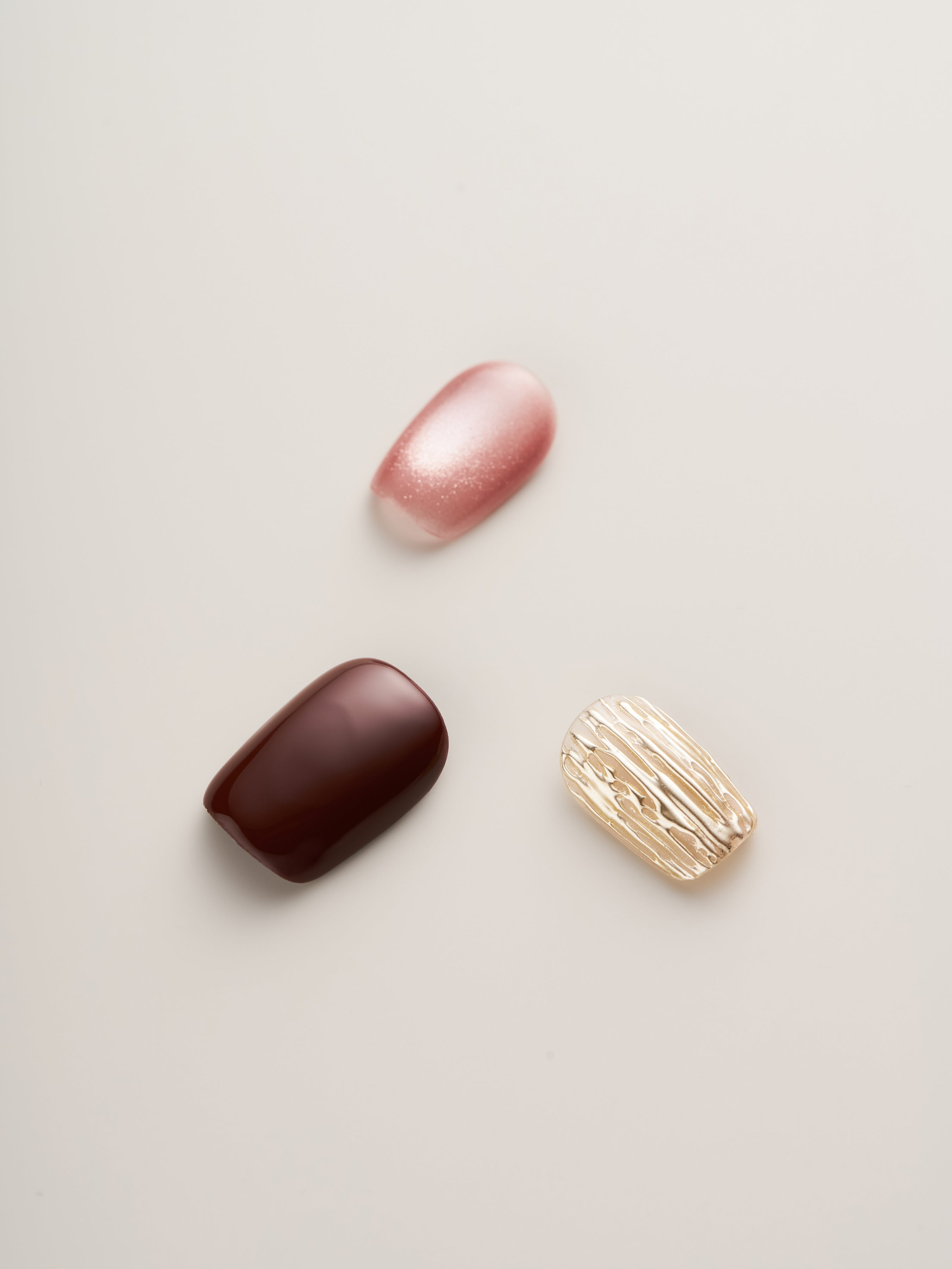Artistic arrangement of Luxe Rosewood & Gold Textured Square Press-On Nails highlighting luxurious gold accents next to rosewood and pink tones, ideal for a chic nail look.