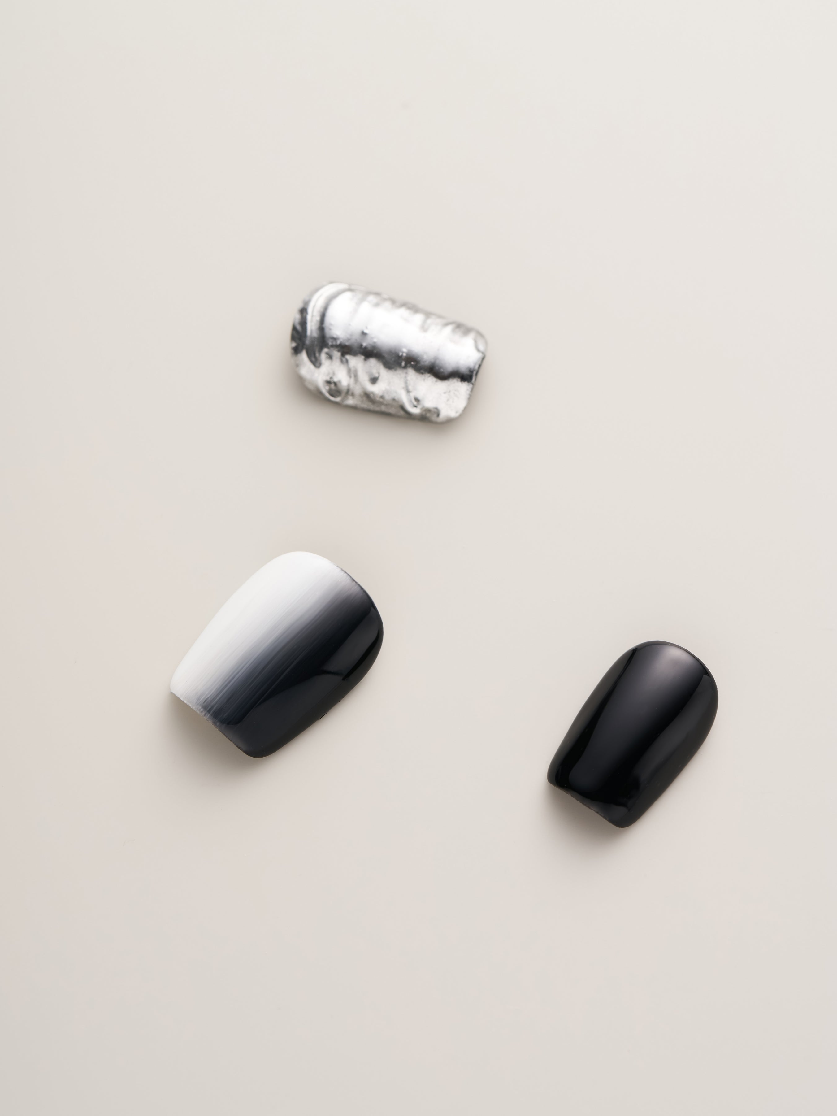 Three distinct Monochrome Metal Press-On Nails showcasing glossy black and gradient white finishes, highlighting the modern aesthetic.