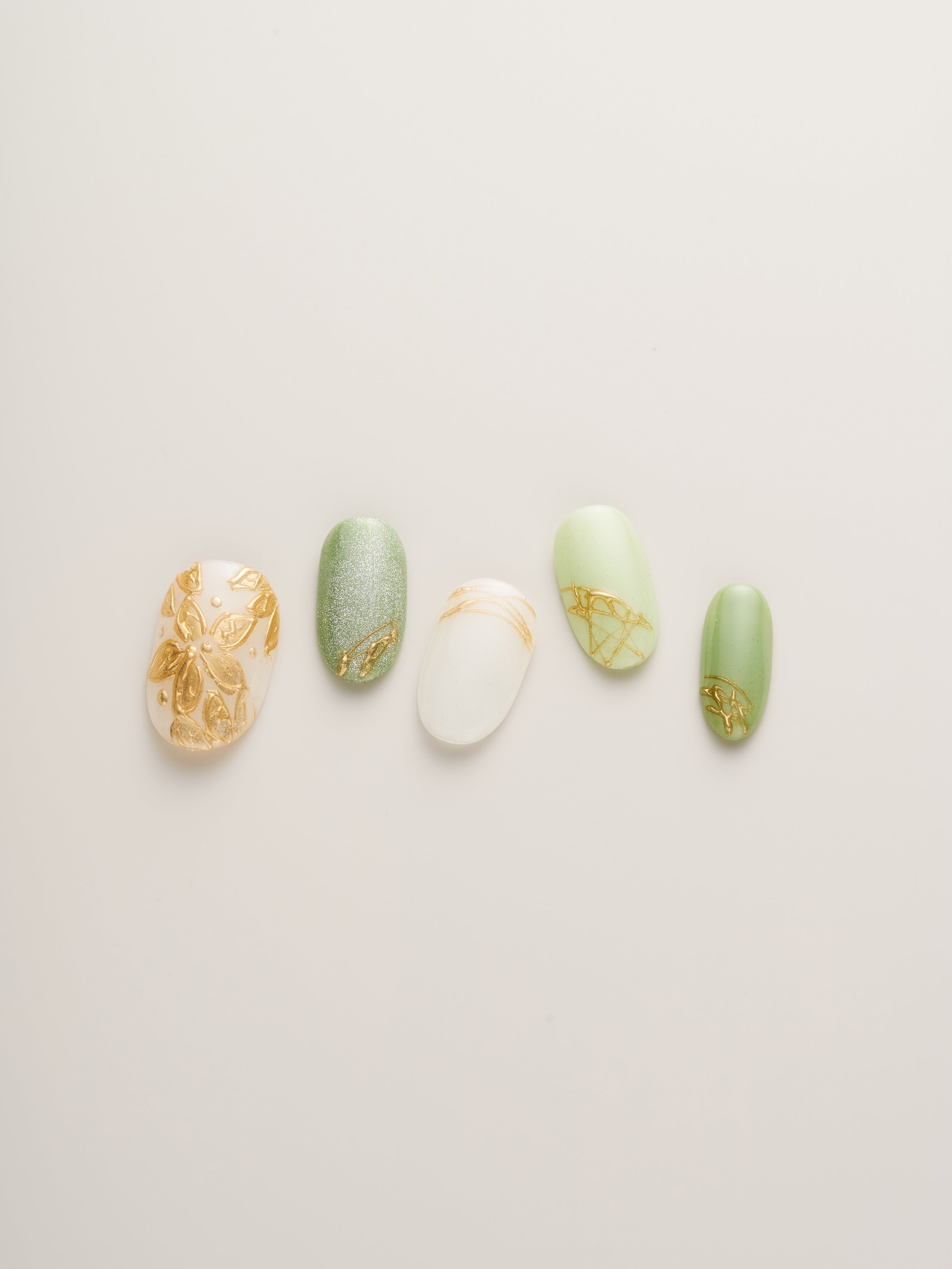 Nailè's Enchanted Garden Press-On Nails arranged in a line, highlighting various shades of green, white, and shimmering gold, ideal for summer events or everyday elegance.
