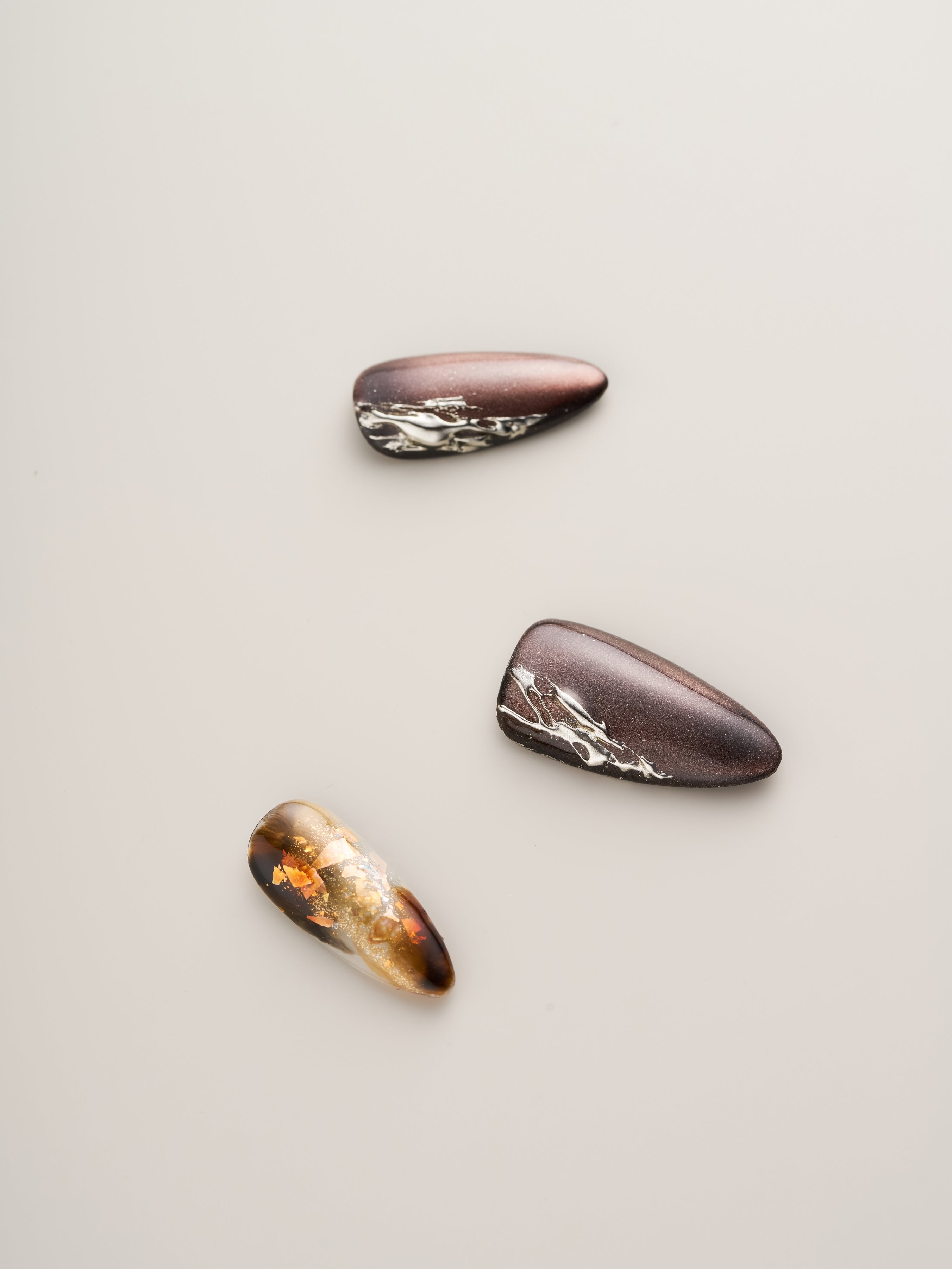 Three stunning Enchanted Garden Press-On Nails displaying elegant gold floral designs on earthy colors, ideal for enhancing any nail art collection.