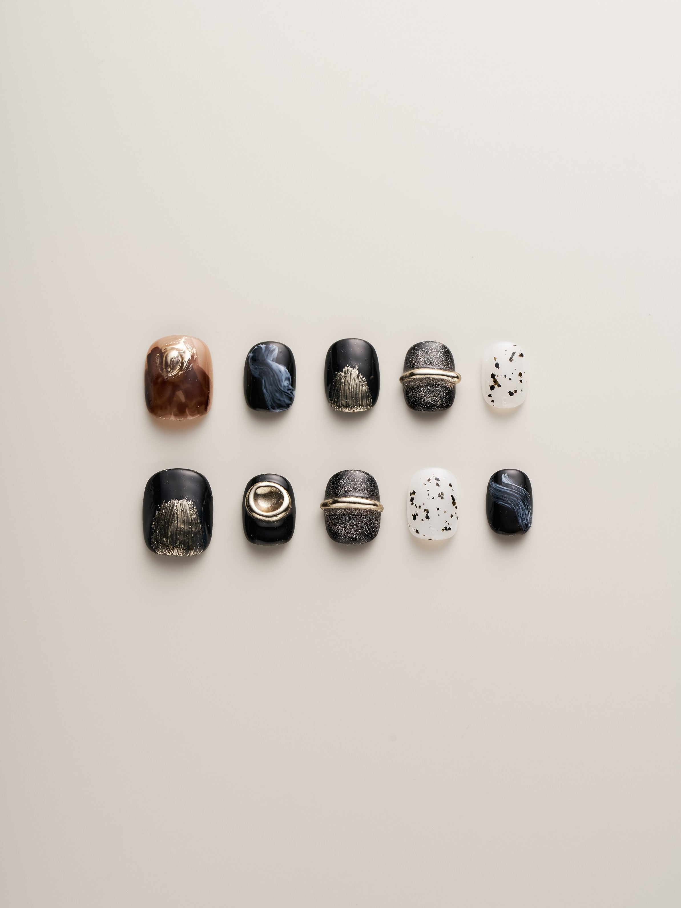 Luxury Metallic Accent Squoval Press-On Nails displayed in a neat row featuring a mix of black, marble, and speckled white designs, highlighted with metallic accents.