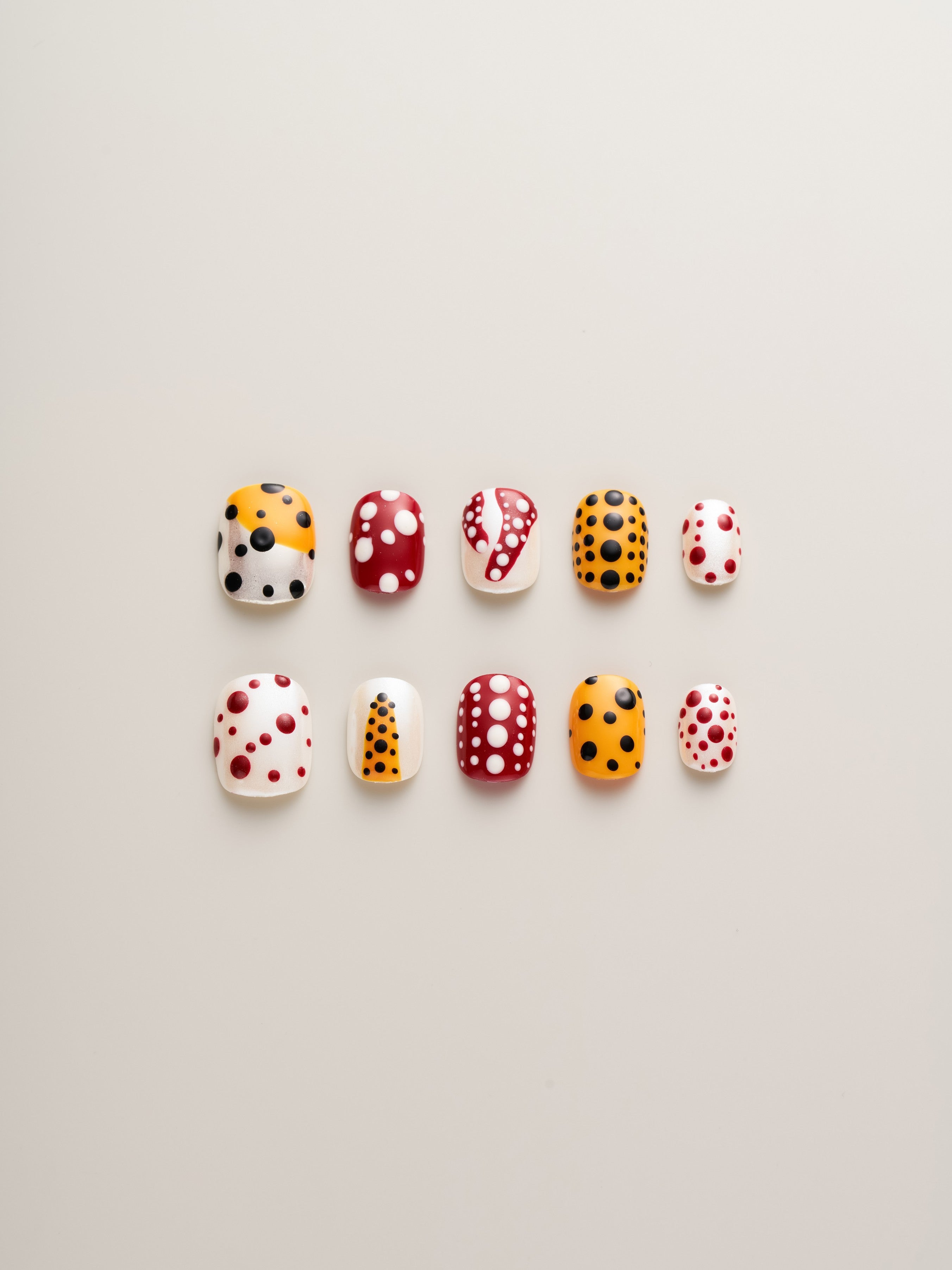 Playful Polka Dot Squoval Press-On Nails featuring colorful designs in red, orange, black, and white polka dots, arranged in a neat display.