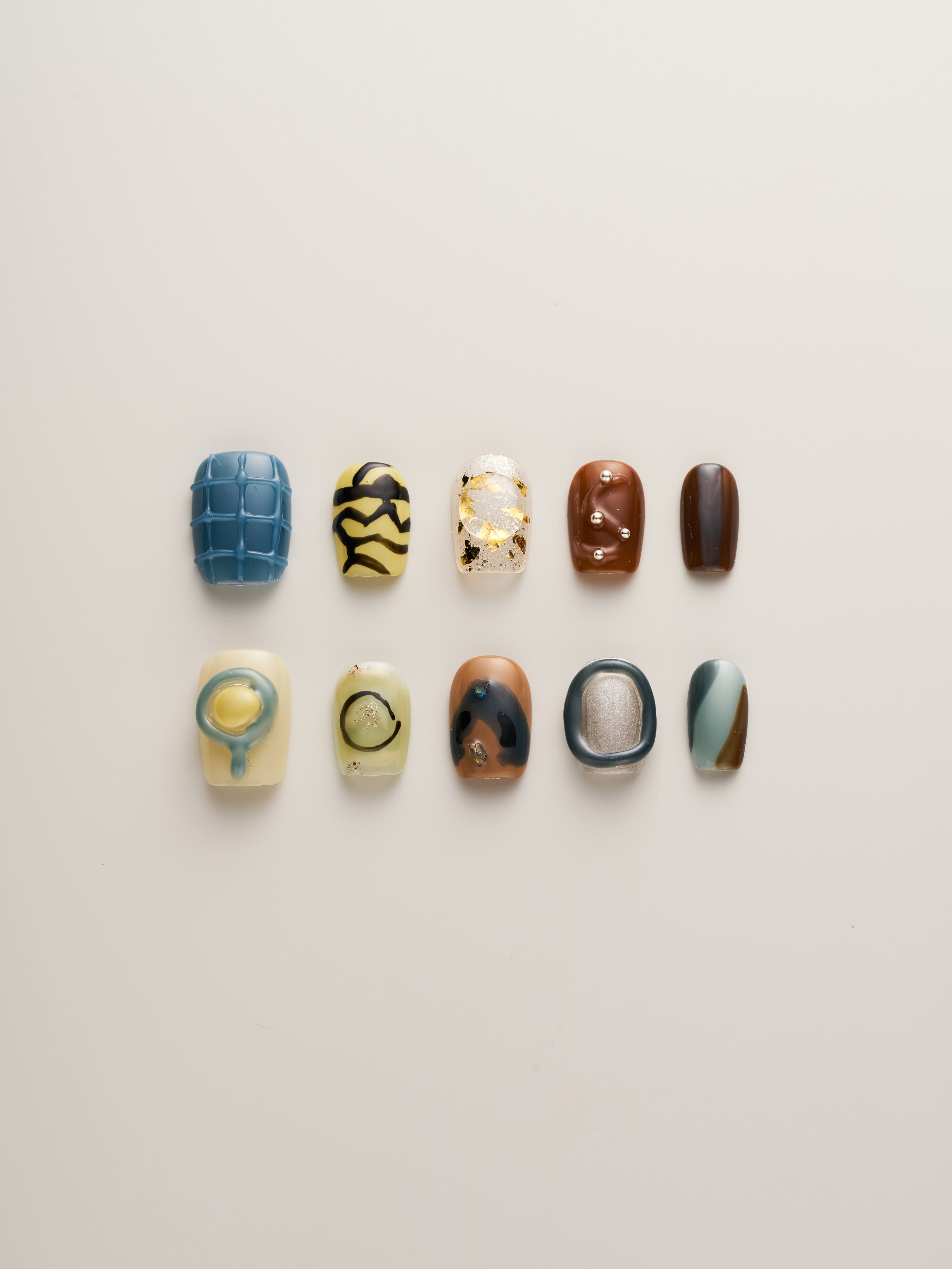 Modern Abstract Squoval Press-On Nails showcasing a variety of artistic designs in earthy tones, textures, and metallic accents arranged beautifully on a neutral background.