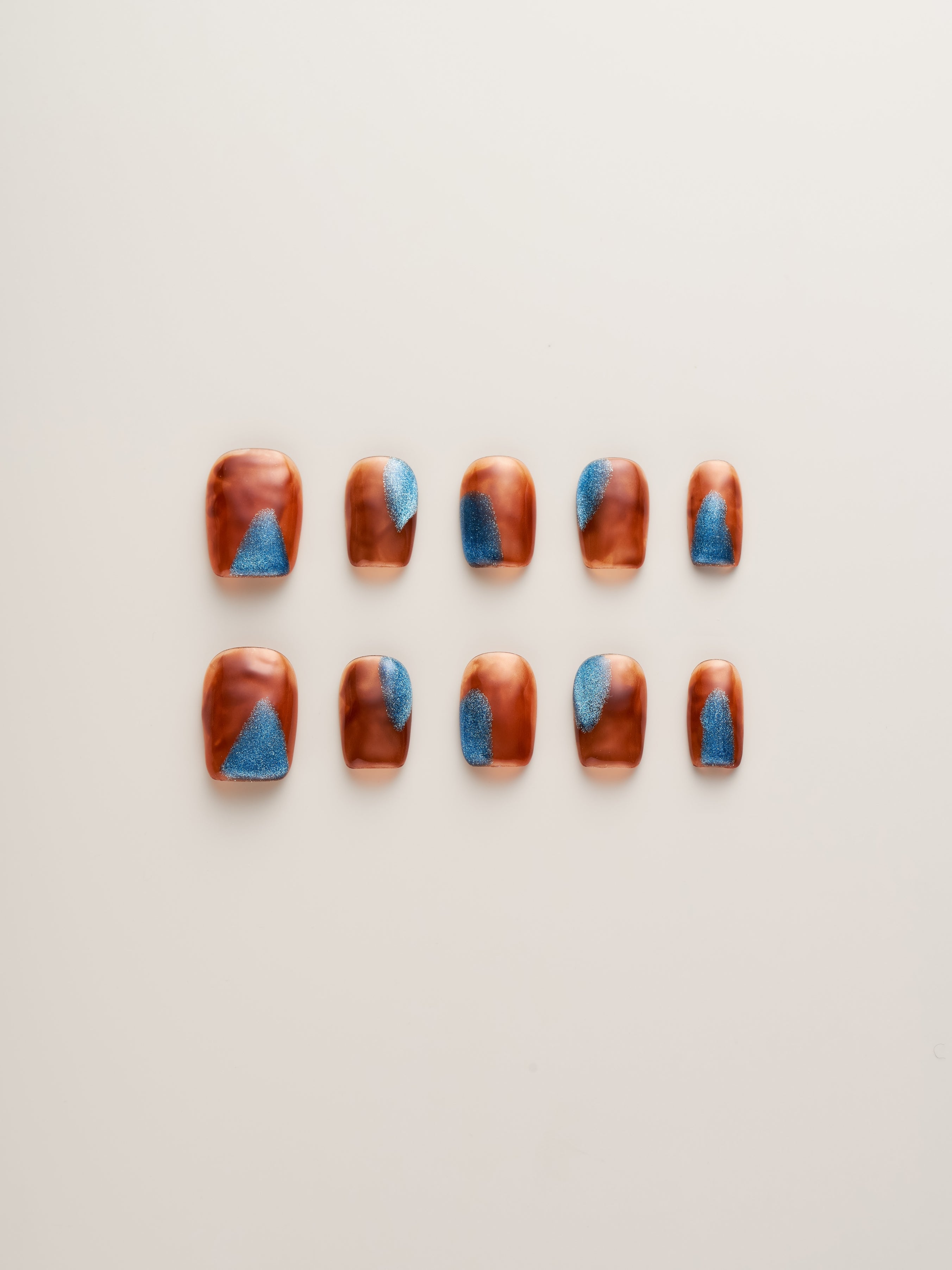 Amber Glow Squoval Press-On Nails showcased in a full set with stunning amber tones and shimmering blue accents.