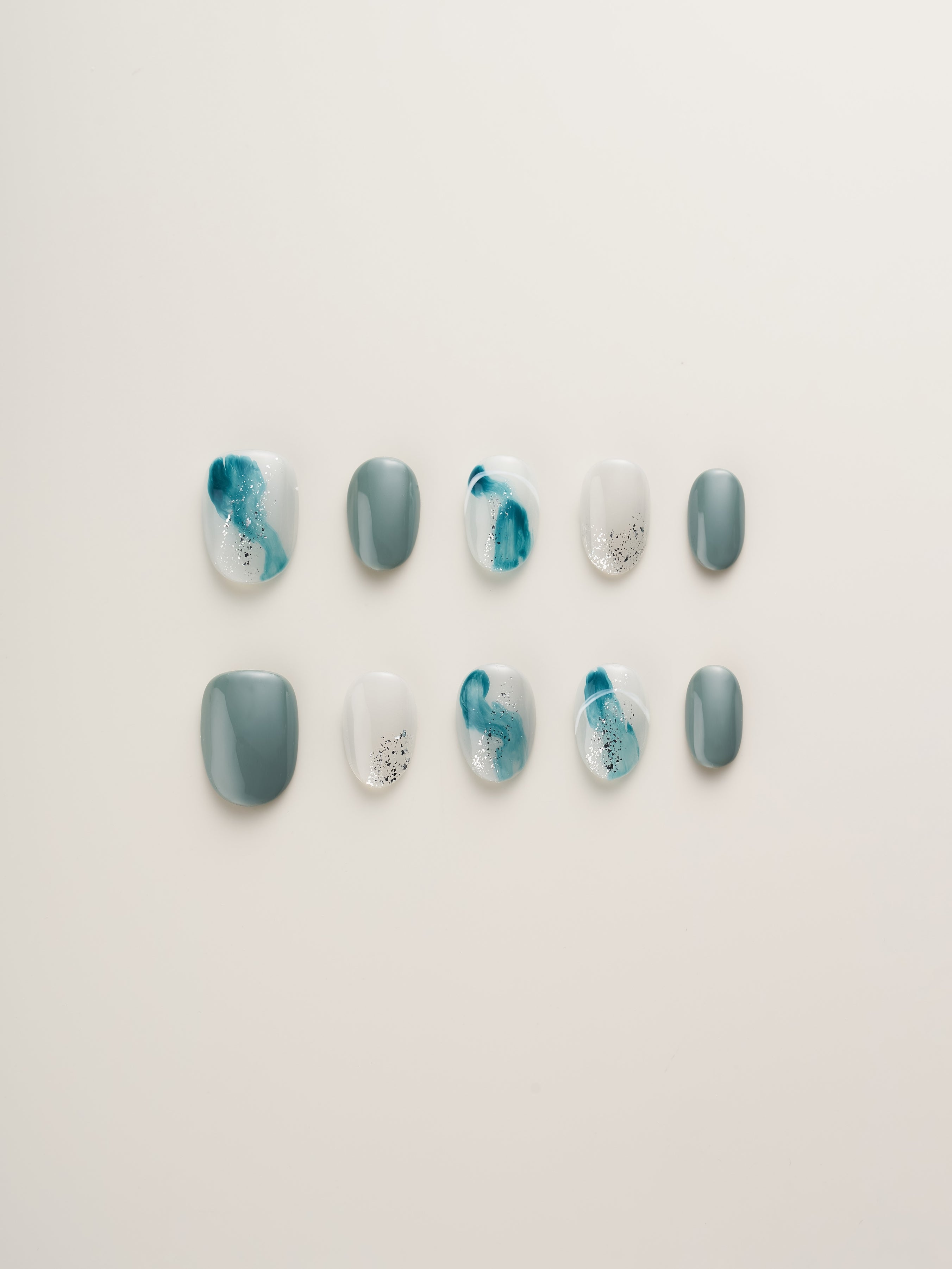 Ocean Breeze Squoval Press-On Nails showcasing a variety of shades from soft gray to blue gradients with sparkling glitter details.