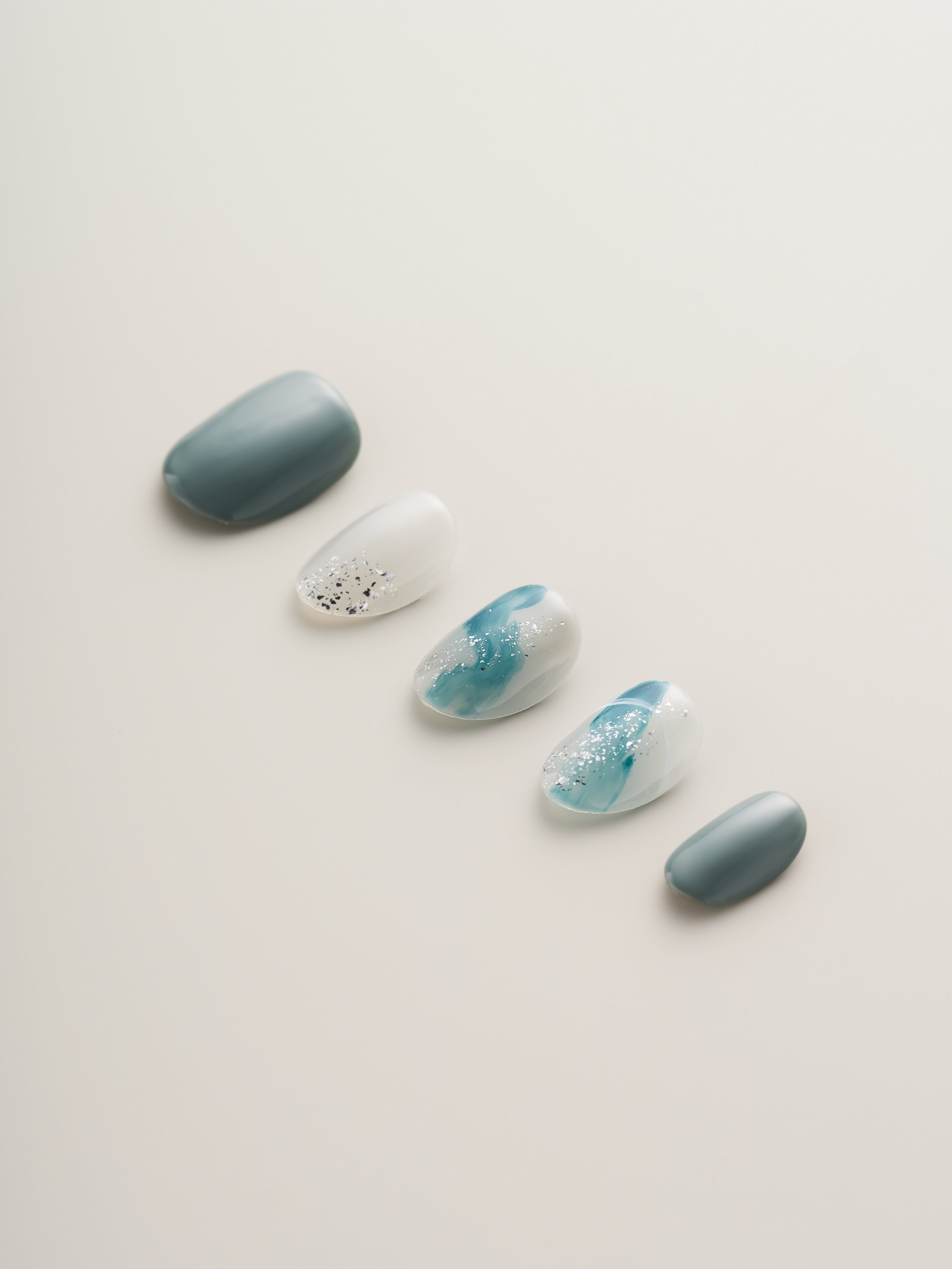 Stylish display of Ocean Breeze Squoval Press-On Nails in a mix of teal, gray, and glitter, ideal for beach vibes.