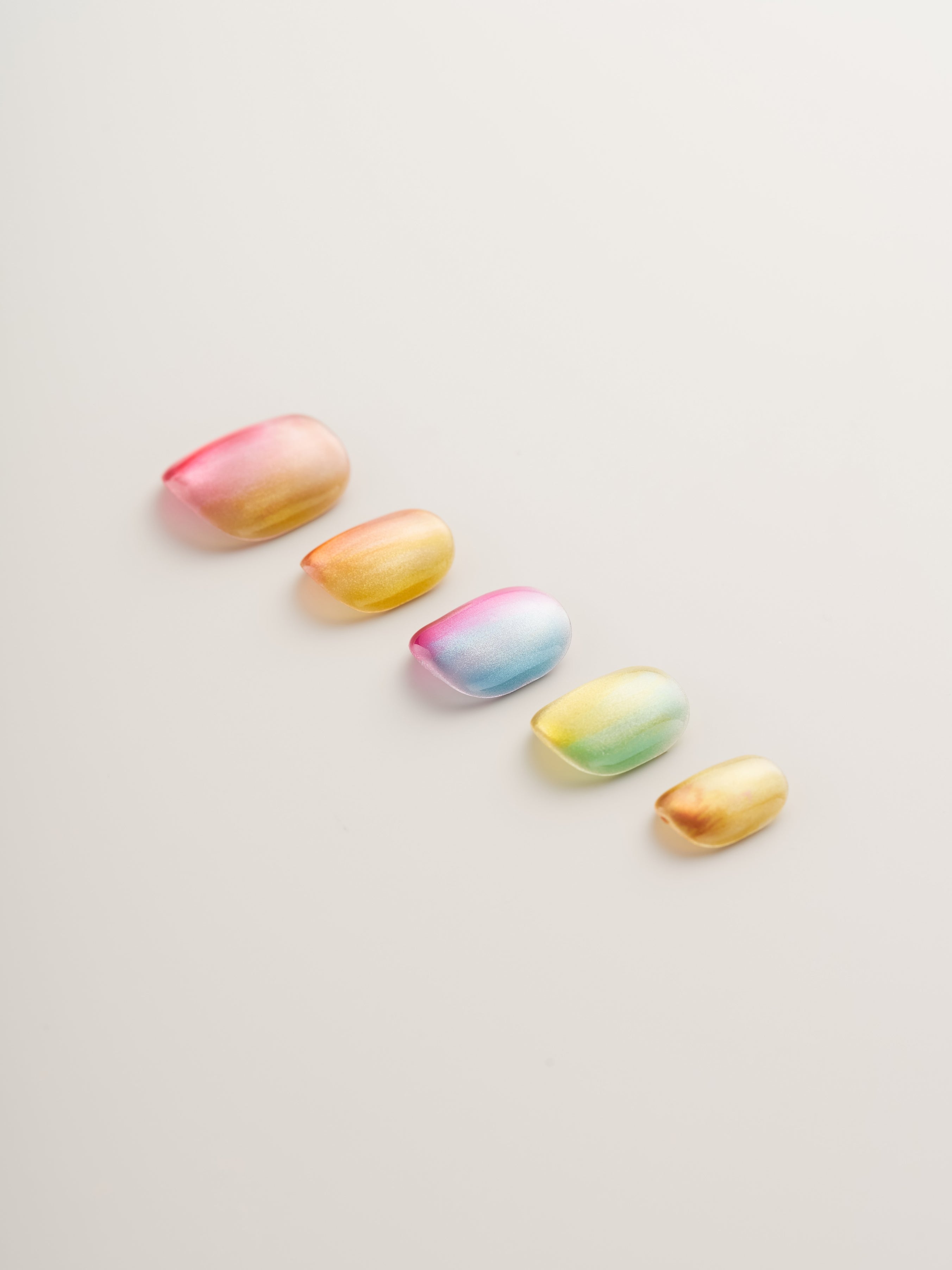 Radiant Sunset Glow Press-On Nails featuring a glossy gradient effect with shades of pink, yellow, and blue. The nails are uniquely shaped, perfect for enhancing your summer look effortlessly.
