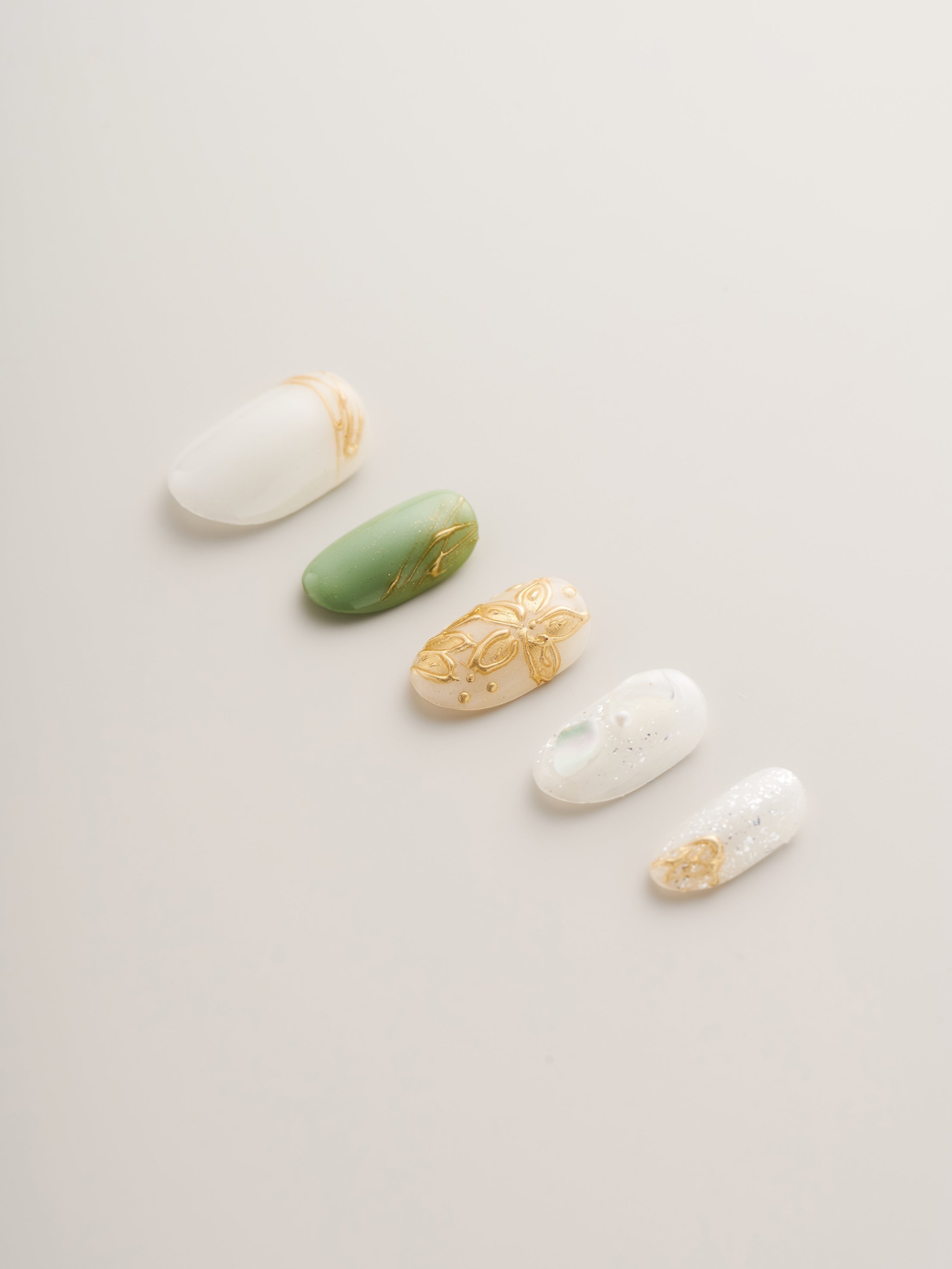 A close-up view of Nailè's Enchanted Garden Press-On Nails featuring intricate gold floral designs on green and white backgrounds, designed for quick at-home manicures.
