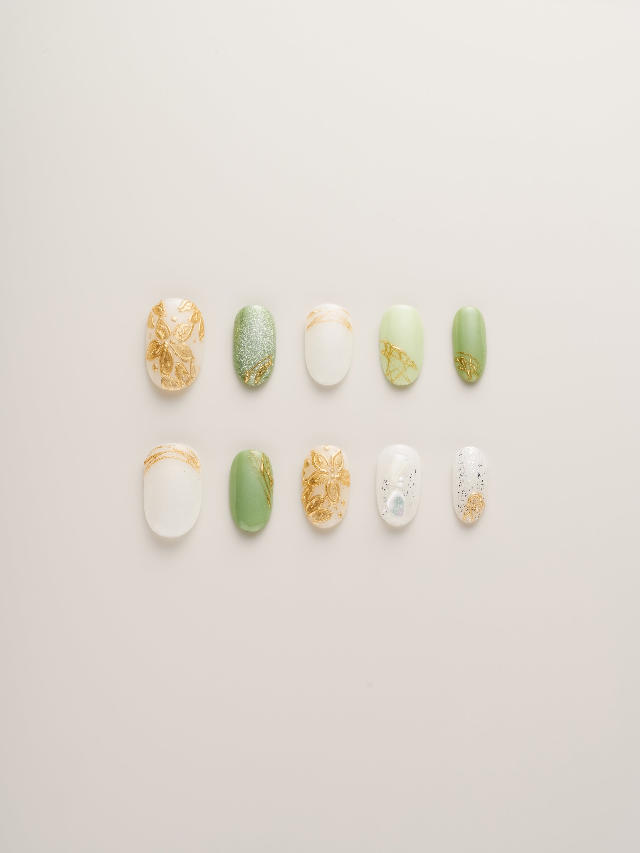 Nailè's Enchanted Garden Press-On Nails showcasing a variety of designs in soft greens and pearlescent whites with gold floral accents, perfect for a chic and sophisticated look.