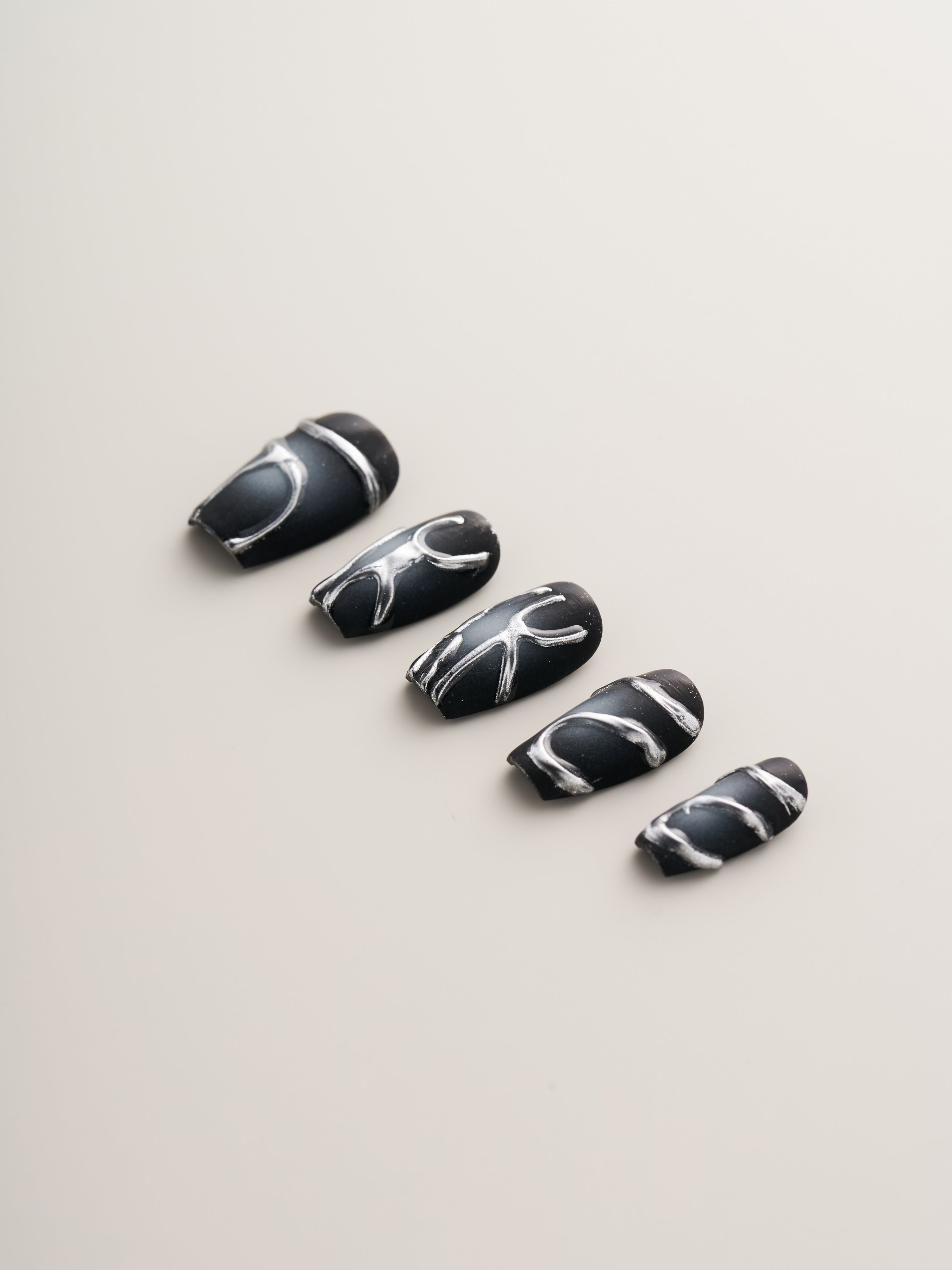 Midnight Noir – Press-On Nails displayed with a close-up view of sleek black nails adorned with striking metallic silver lines, emphasizing a modern aesthetic.