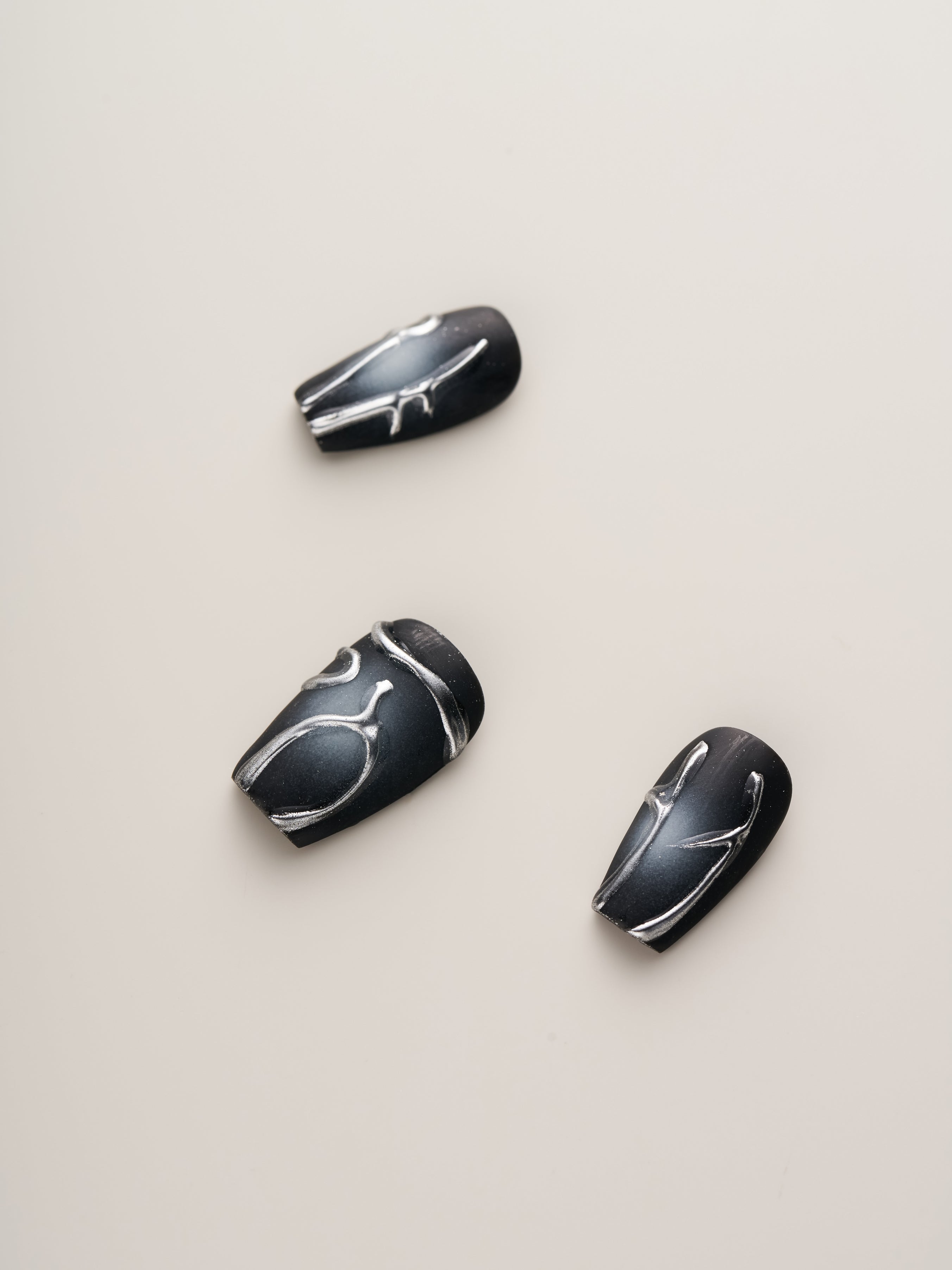 Midnight Noir – Press-On Nails showcasing individual artfully designed black nails with silver detailing, offering a chic and avant-garde finishing touch.