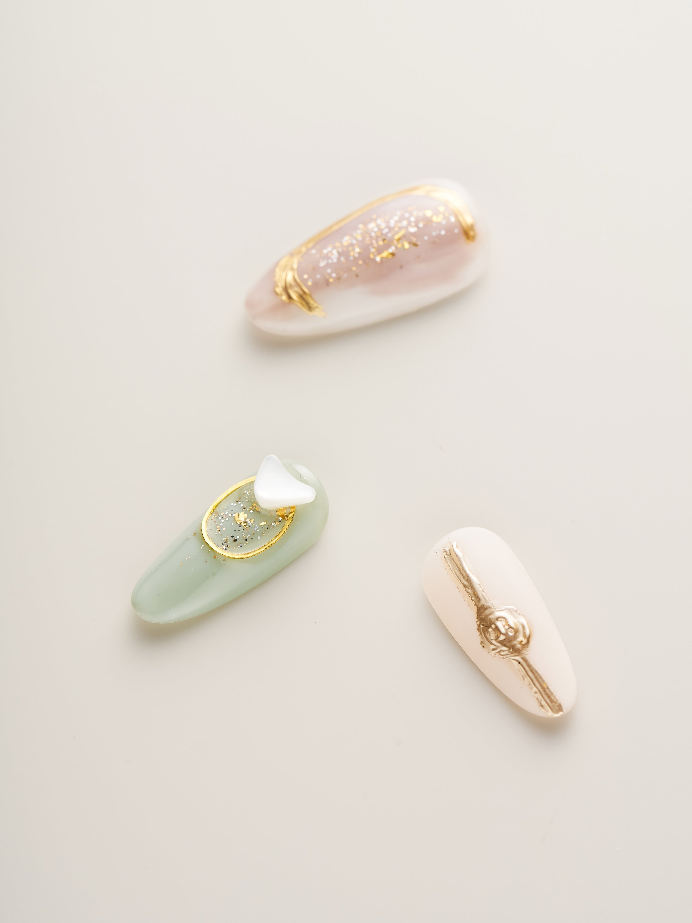 Close-up view of individual Celestial Harmony Press-On Nails showcasing soft pastels and intricate gold details on a neutral backdrop.