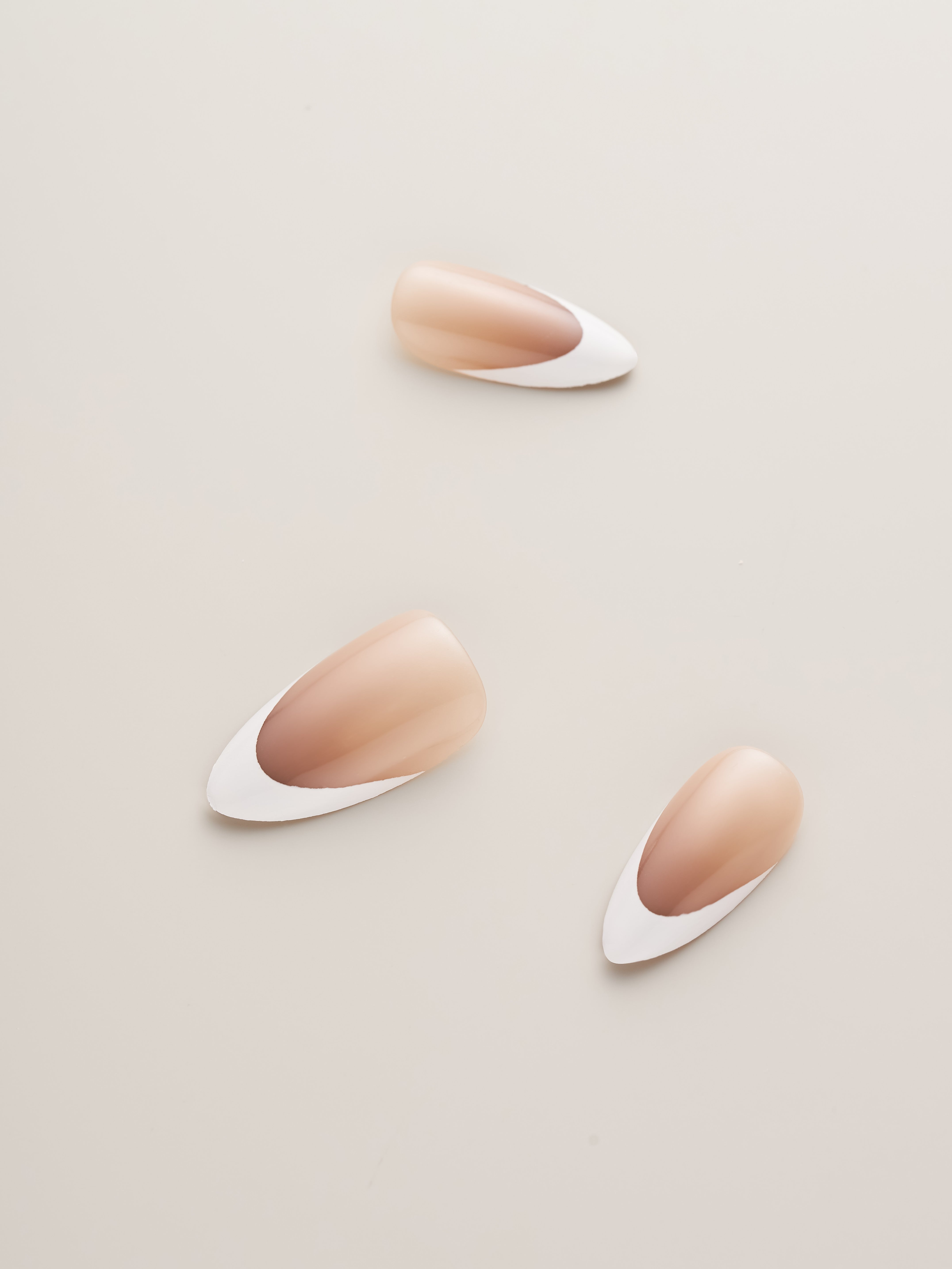 Three Classic Nude and White French Tip Almond Press-On Nails in different sizes, ideal for customizing your nail look effortlessly.