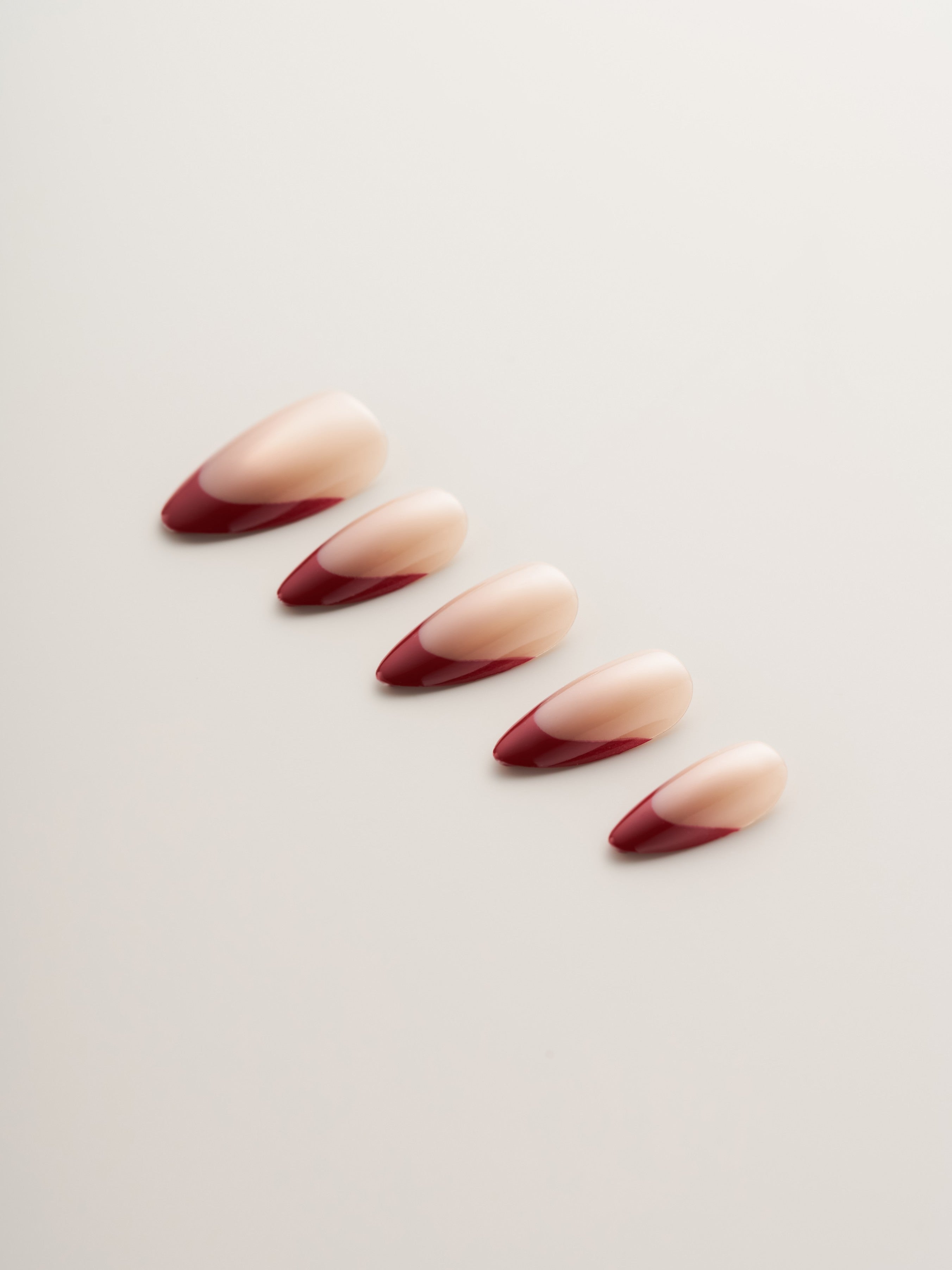 Five Chic Red French Tip Almond Press-On Nails arranged in a row against a neutral backdrop, highlighting their stylish almond shape and bold red tips.