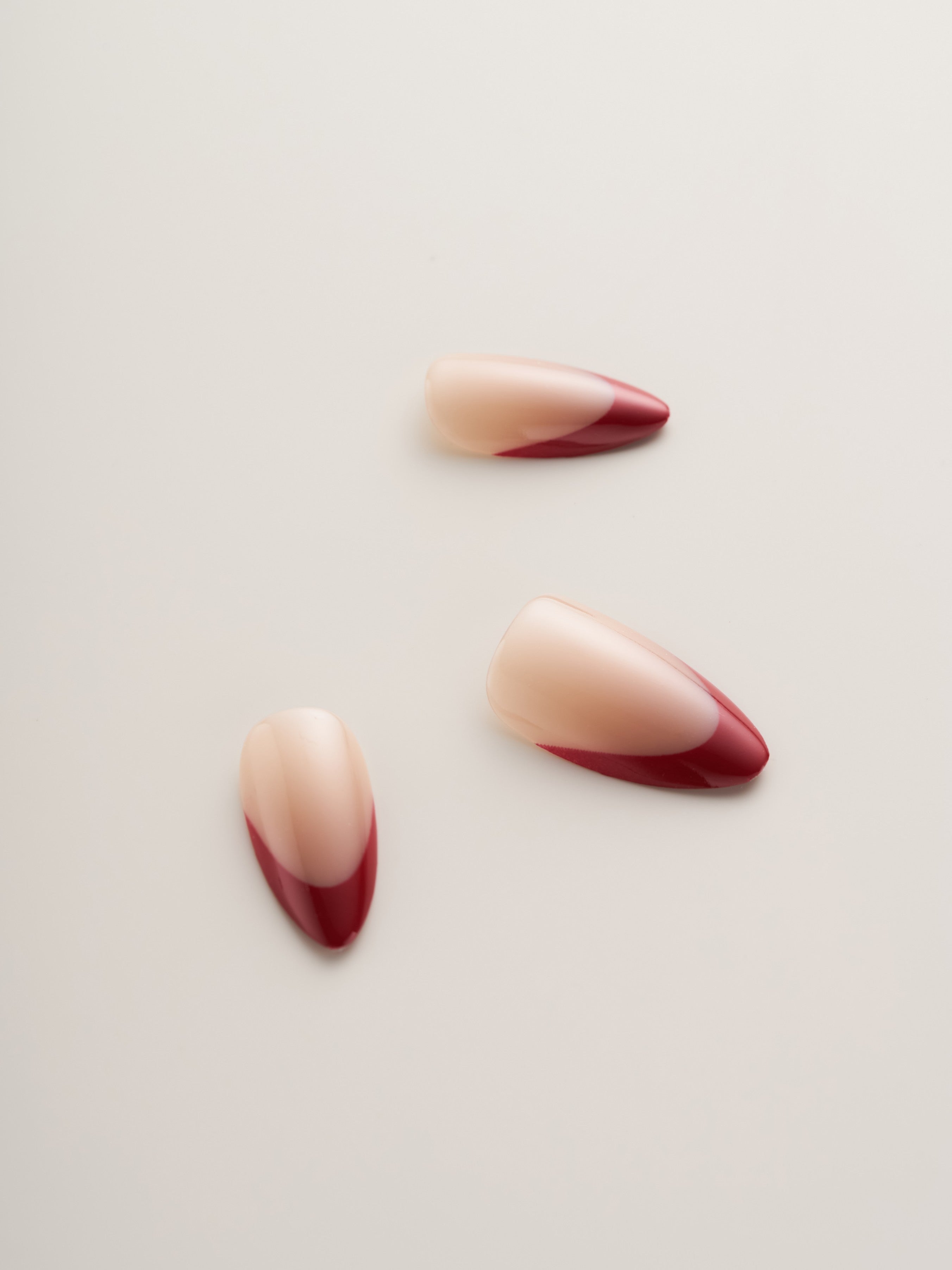 Three Chic Red French Tip Almond Press-On Nails on a light surface, emphasizing the harmonious blend of milky white and striking red tips.