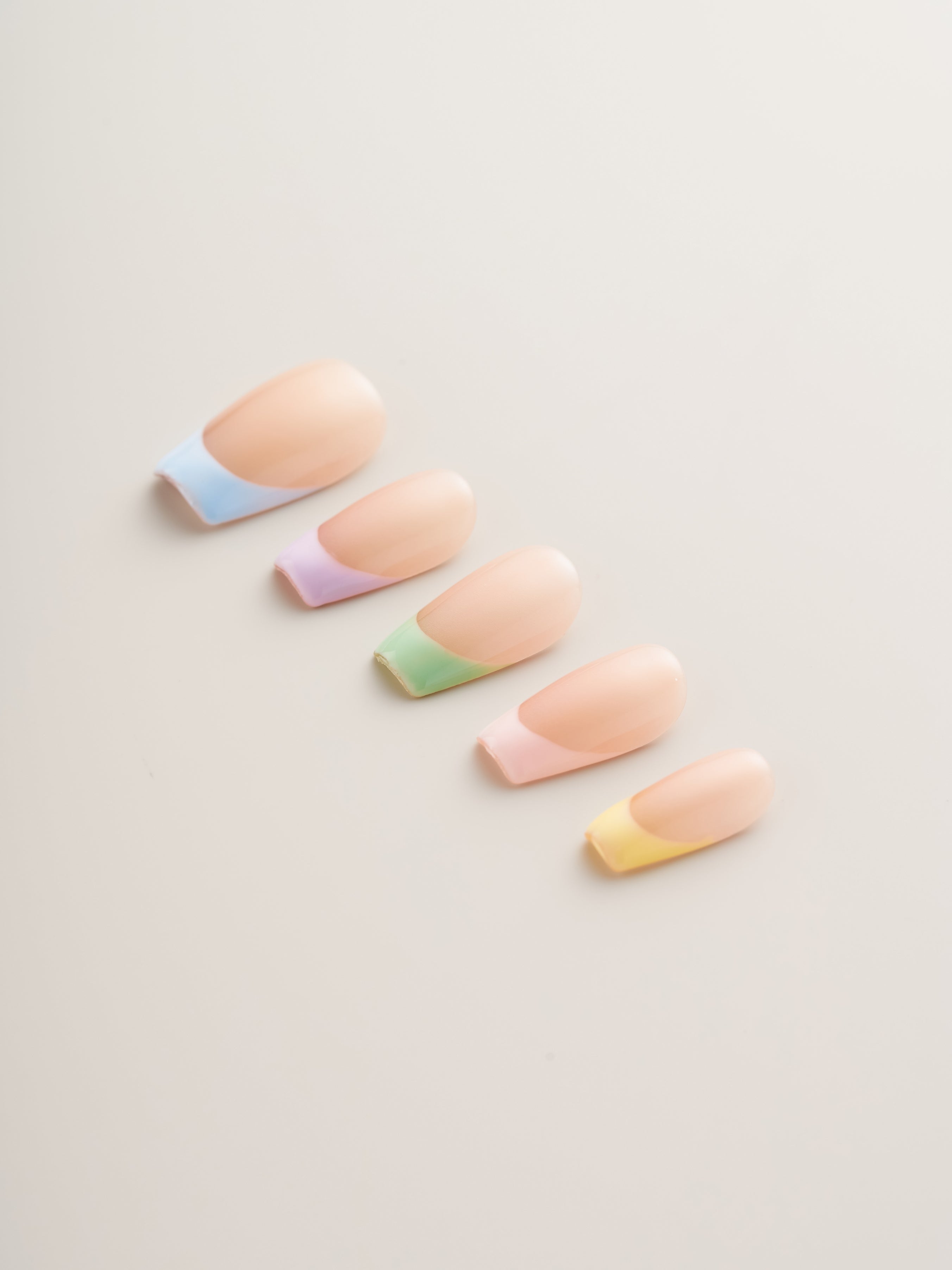 Close-up view of pastel French tip press-on nails, showcasing shades of blue, pink, green, and yellow on a nude base from the Pastel Chic collection.